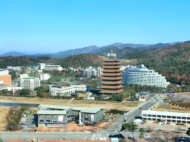 A multi storey wooden structure with tiered roofs, among town buildings and hills