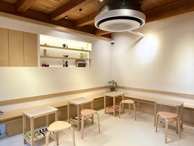 A minimal space with wooden ceiling beams, a bench along the wall and pale stools