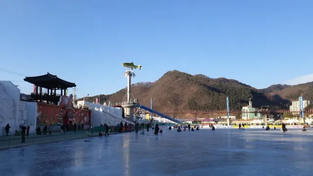 A wide frozen river with visitors on the ice, a fish sculpture and hills in the background