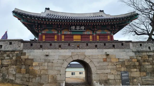 An arched stone gate within a wall, with a brightly painted wooden pavilion above it