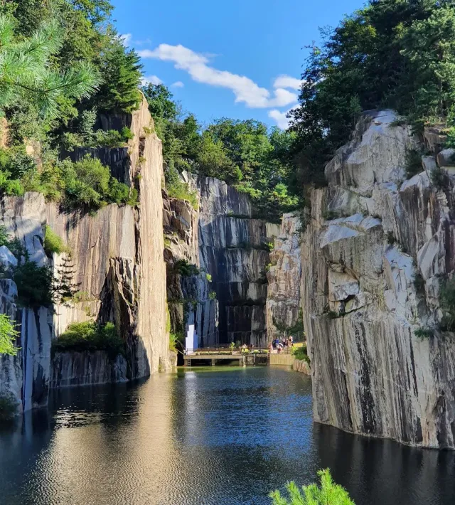 Straight quarried stone walls dropping into a greenish lake, trees at the top