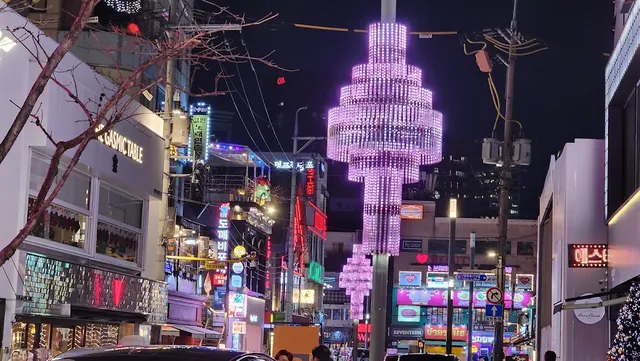 A street at night with neon signs and a huge purple chandelier of lights hanging above it