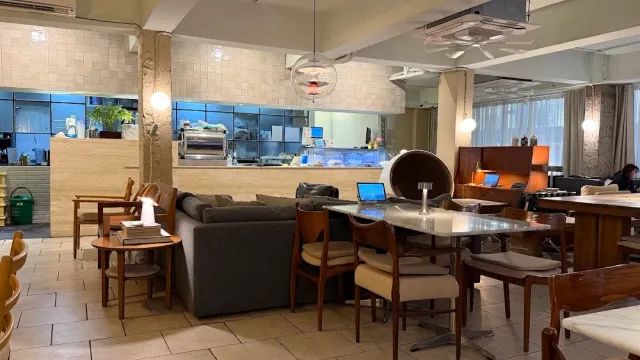 A space with a grey sofa, wooden chairs, a metal table and an open laptop