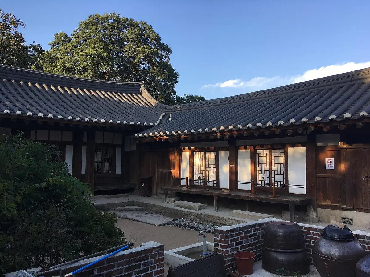 Courtyard of a traditional house with curved tiled roofs, glowing paper doors and clay jars in the corner