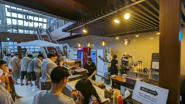 A food counter in a tall space with hanging lamps and people waiting in line