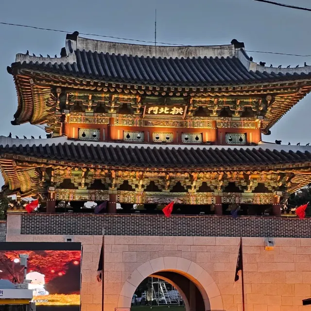 A two-storey fortress gate lit at dusk, with red flags along the wall
