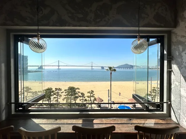 A large window onto a beach, a long bridge and the sea, with two glass lamps and a seating counter