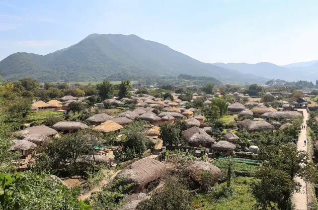 Clustered thatched roof houses in a valley with a mountain behind