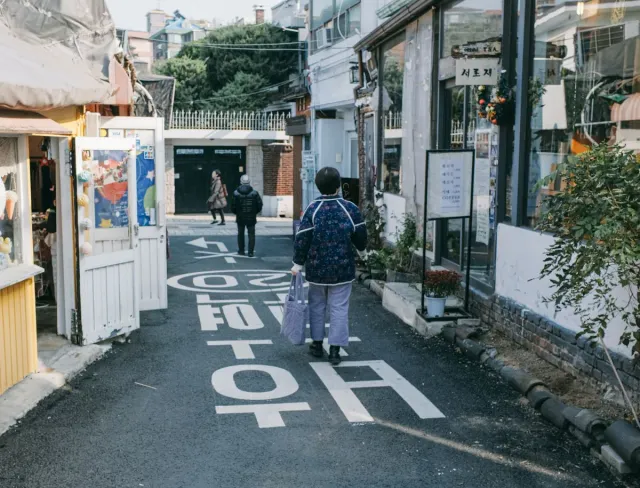 A narrow alley with small shops, large lettering on the road and pedestrians