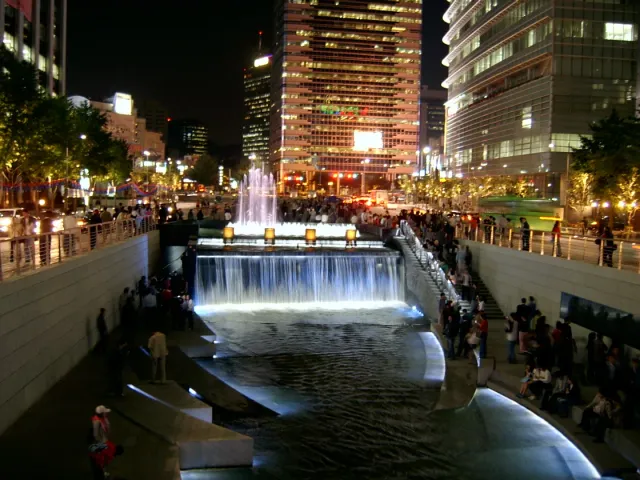 A lit waterfall in an urban channel with stone steps and city lights at night