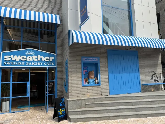 A light blue front with striped awnings, blue doors and a sign above the entrance