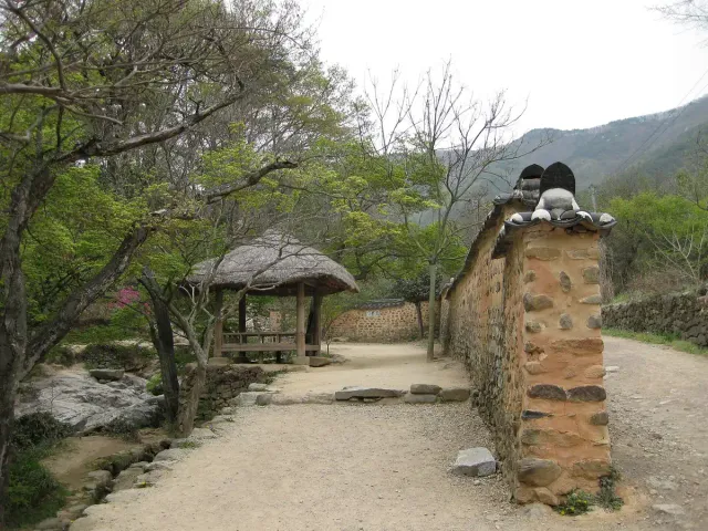A thatched pavilion beside a low stone wall in a bamboo grove