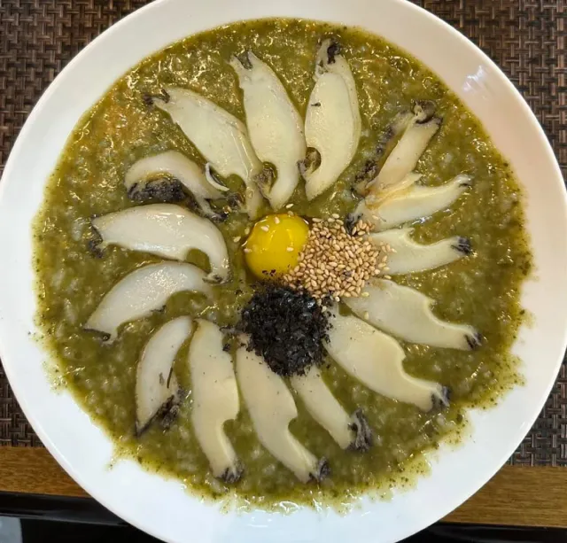 Greenish porridge in a white bowl with white slices arranged in a circle and a yolk