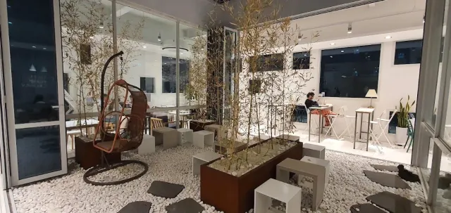 A white space with gravel on the floor, bamboo planters, a hanging chair and cube stools