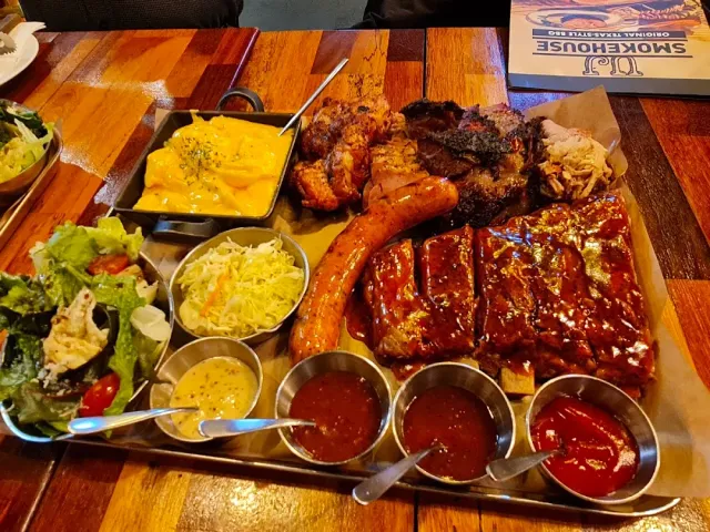 A large platter of ribs, sausage and smoked meat with creamed corn, salad and sauces