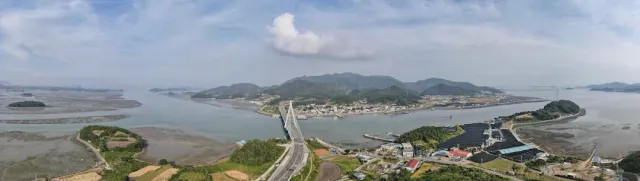 A panorama of a shallow bay with a bridge, a coastal town and green hills