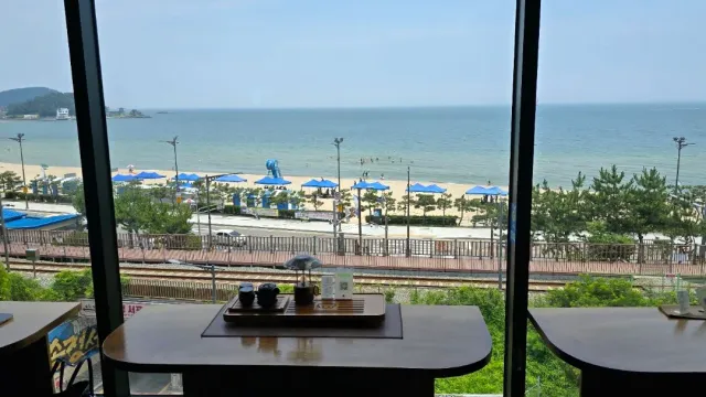 A view from a window onto a beach with blue parasols and the sea, and a tea tray on the table