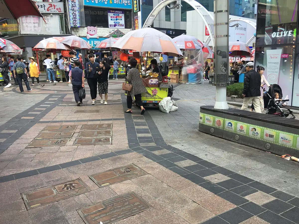 A paved square with handprint plaques and street food stalls under parasols