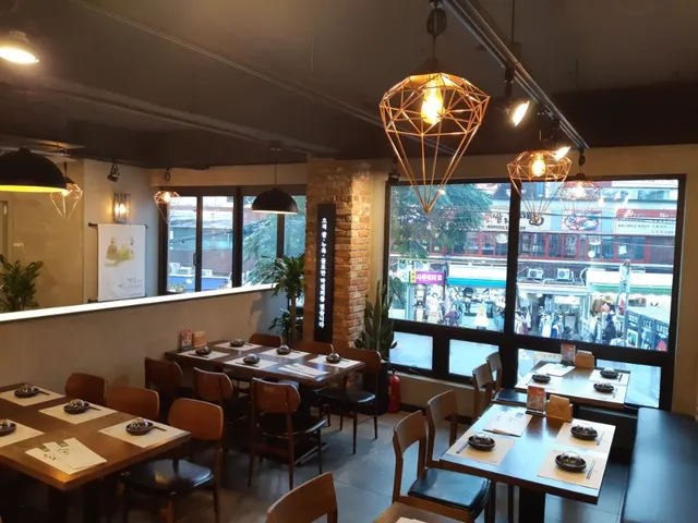 A hall with set wooden tables, hanging lamps and large windows onto a busy street