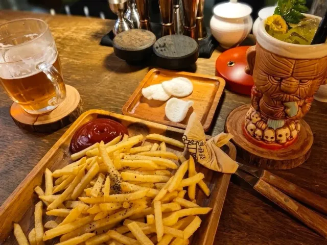 A tray of fries with sauce, a glass of beer and a cocktail in a carved mug on a wooden table