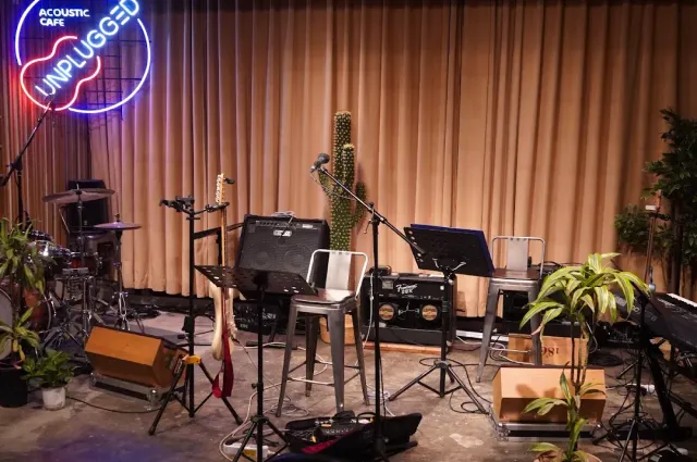 A stage in front of a beige curtain with a guitar, amplifiers, music stands and a neon sign