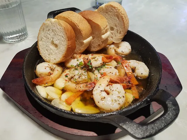A cast iron pan with shrimp and garlic cloves in oil, and slices of toasted bread on top