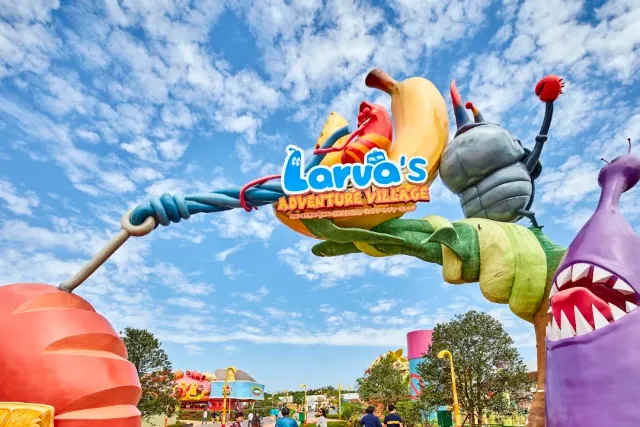 A sculpted entrance arch shaped like colorful insects against a lightly clouded sky