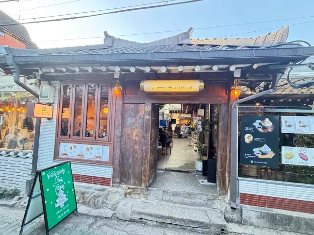 A traditional gate with a tiled roof and red lanterns, with a courtyard and tables behind it