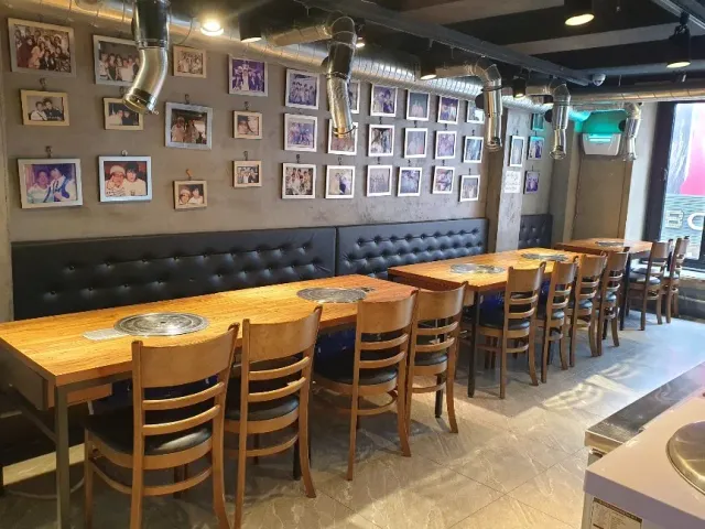 A restaurant hall with wooden tables holding sunken grills, and a wall of framed photos