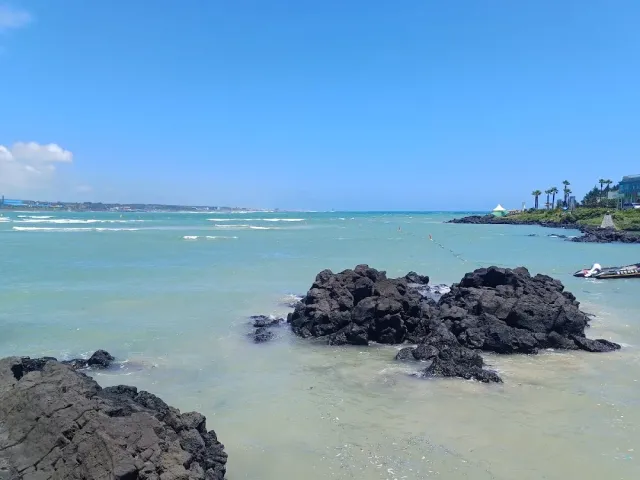 Shallow turquoise water with black basalt rocks and a pale sand shore