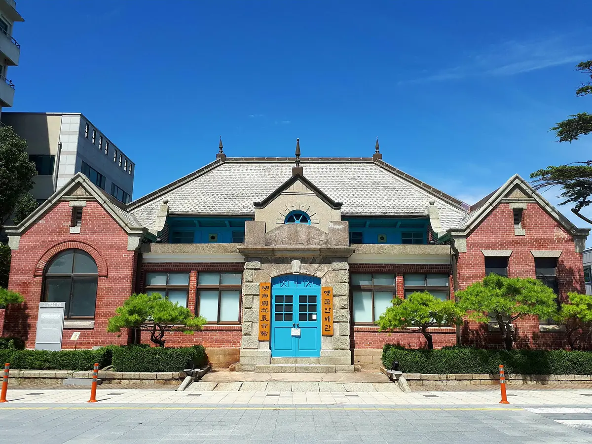 Red brick colonial era building with a bright blue door and clipped pine trees under a blue sky
