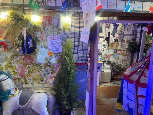 A corner crowded with decorations, floral wallpaper, a white rocking horse and notes on the wall