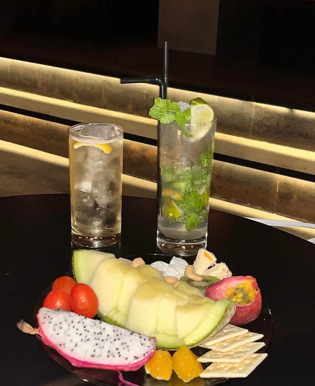 Two cocktail glasses with mint and lemon, beside a plate of fresh fruit and crackers