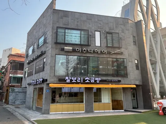 A corner building clad in grey stone with signs and a yellow shopfront on the ground floor