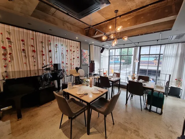 A bright space with a grand piano, set tables and a curtain wall decorated with red flowers