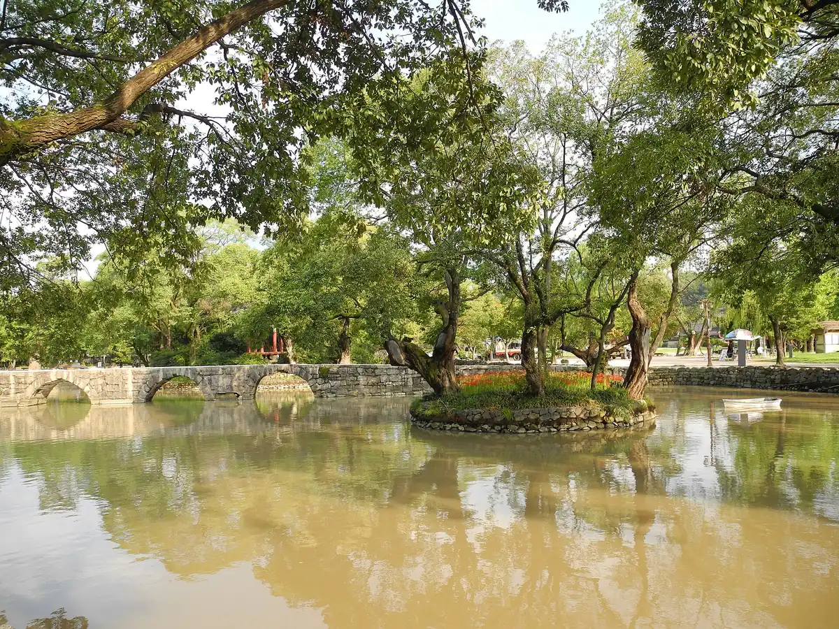 Garden lake with a small tree covered islet at its centre and an arched stone bridge behind