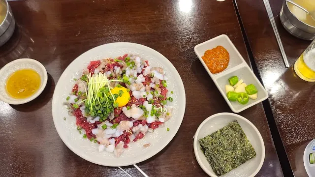 A plate of chopped raw beef with octopus, an egg yolk and greens, beside small side dishes