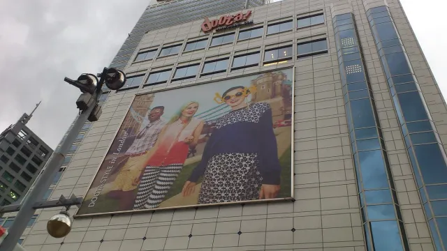 The facade of a multi storey fashion mall with a huge banner and a glass entrance