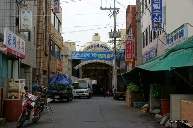 A market lane under a green canopy lined with shops and Korean signage