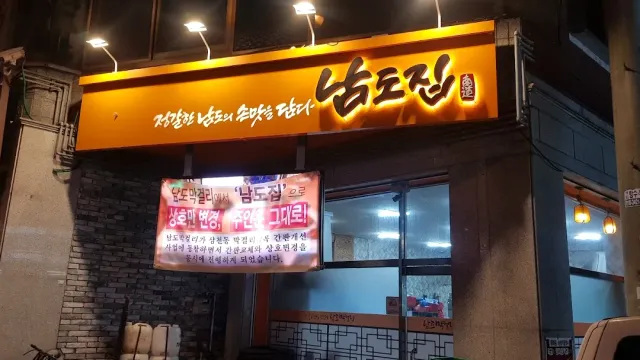 A restaurant front at night with a lit orange sign and a cloth banner beneath it