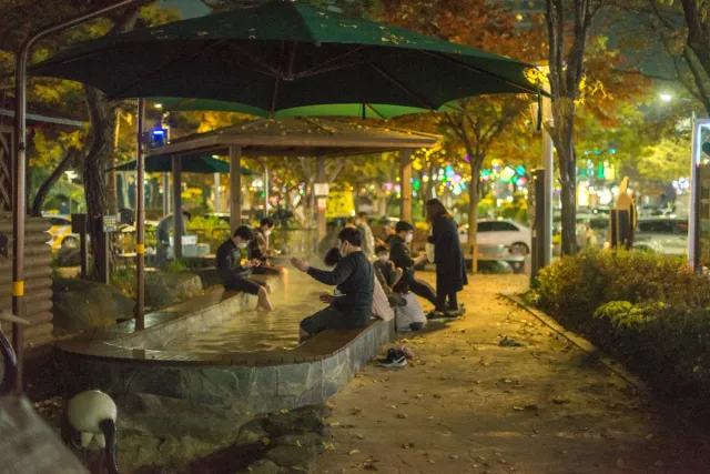 Visitors sitting and soaking their feet in a warm water basin under parasols in the evening