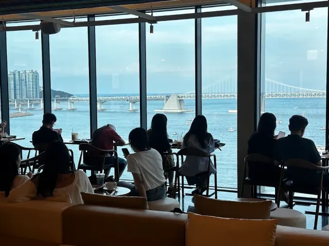 A glass wall facing the sea and a long bridge, with guests seated in front of the view