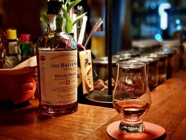 A whisky bottle beside a tasting glass on a wooden counter in dim lighting