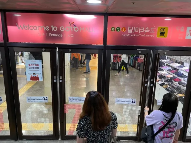 Glass doors of an underground entrance with a pink sign and customers walking in