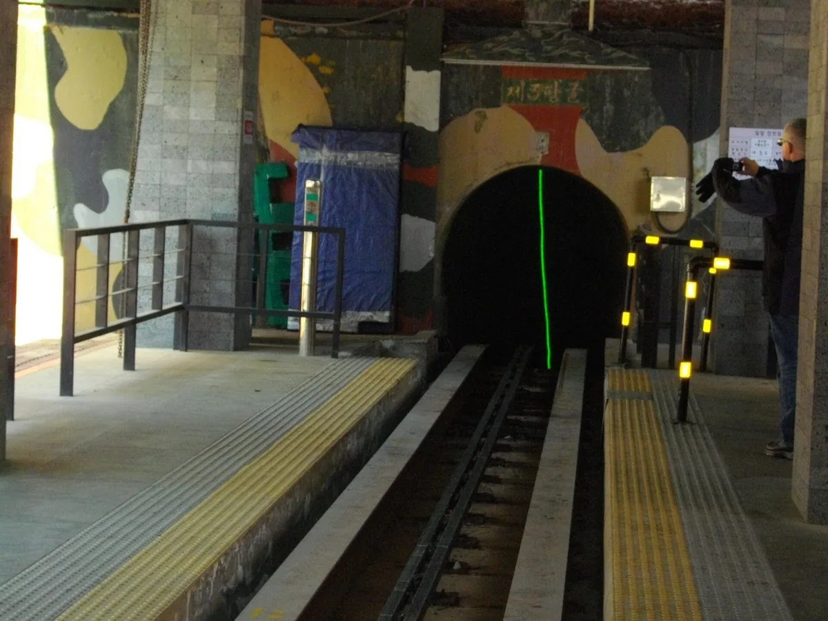 A dark tunnel mouth with a rail track descending into it, between camouflage painted walls