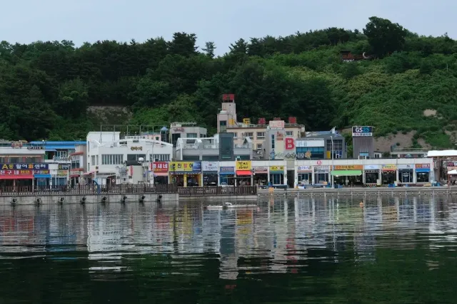 A row of colorful shops on a harbor quay, reflected in greenish water