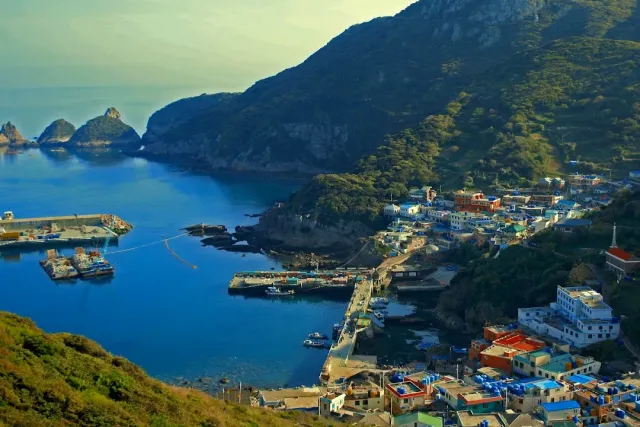 A harbor village with blue roofs on a steep slope above a bay and rocks in the sea