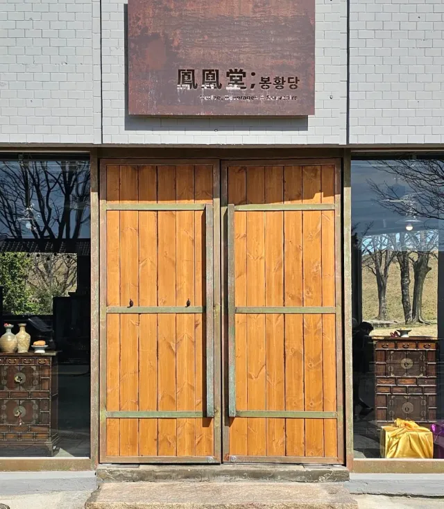 Large double wooden doors with a rusted metal sign above them and display windows on either side