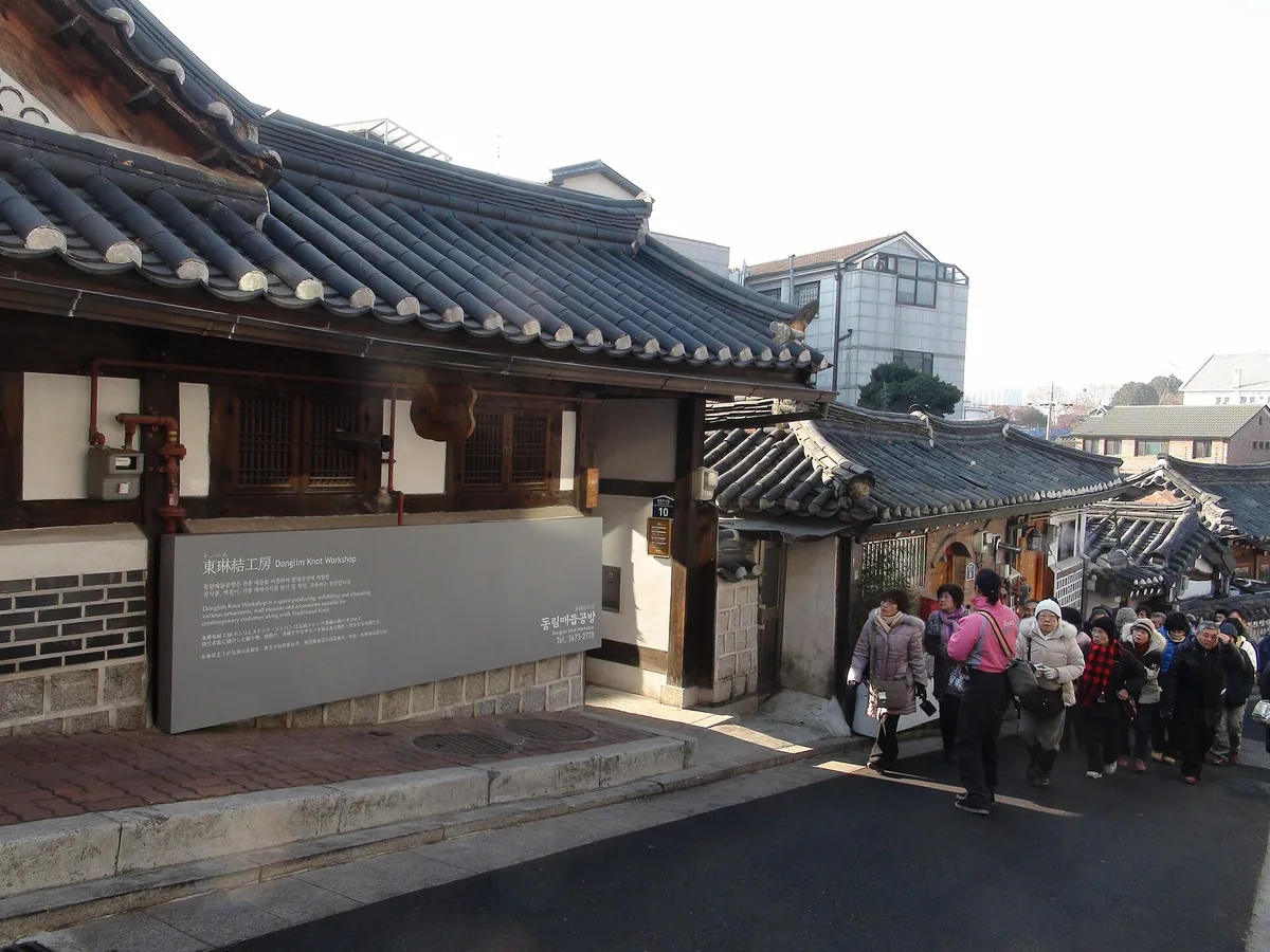 A sloping lane between tiled hanok roofs with visitors walking up it