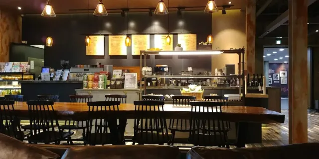 A space with long wooden tables, black chairs and a counter with menu boards